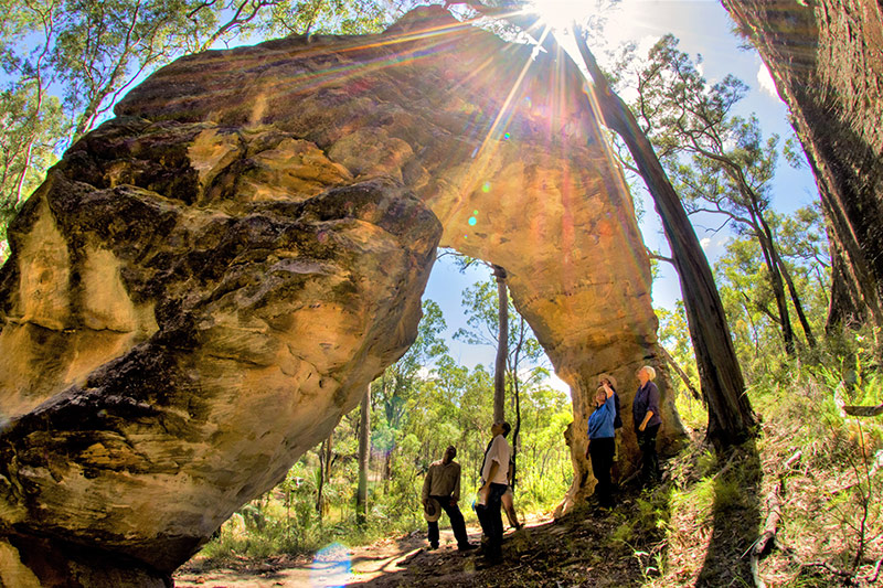 People looking up at large arched rock formation